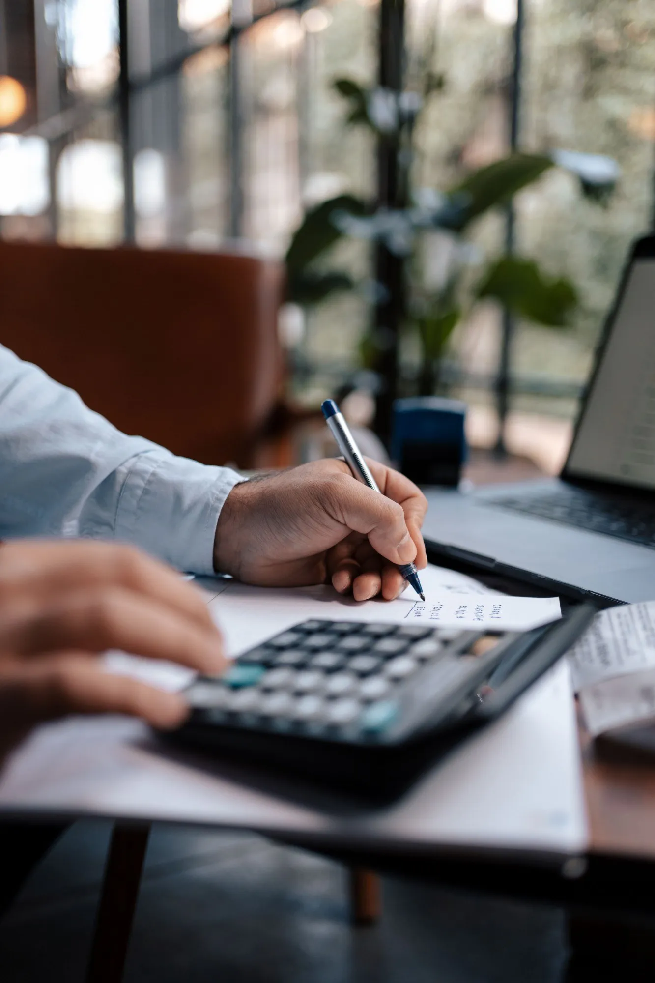 Someone working through figures with a calculator, pen and laptop